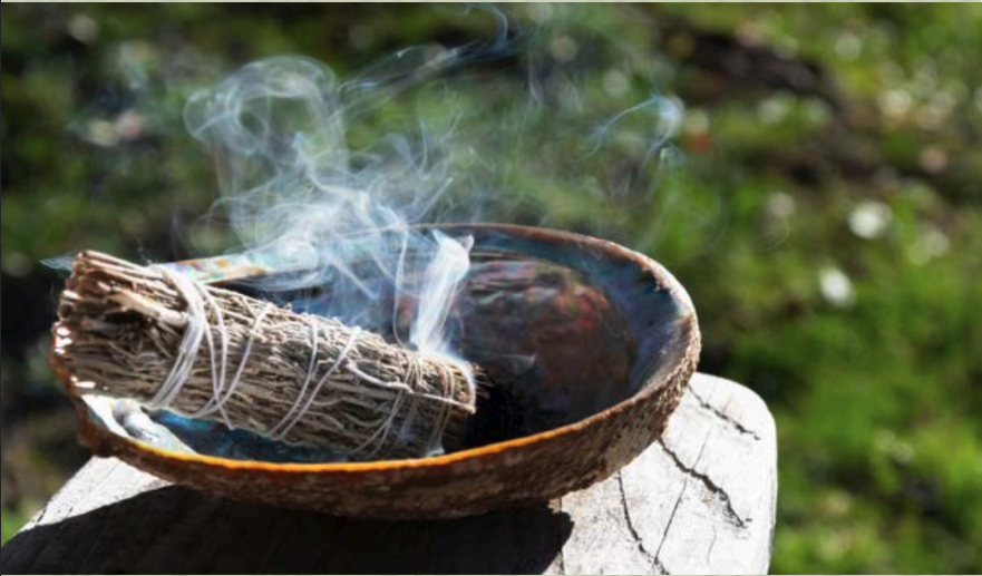 Smudge bowl with burning sage against a forest background.